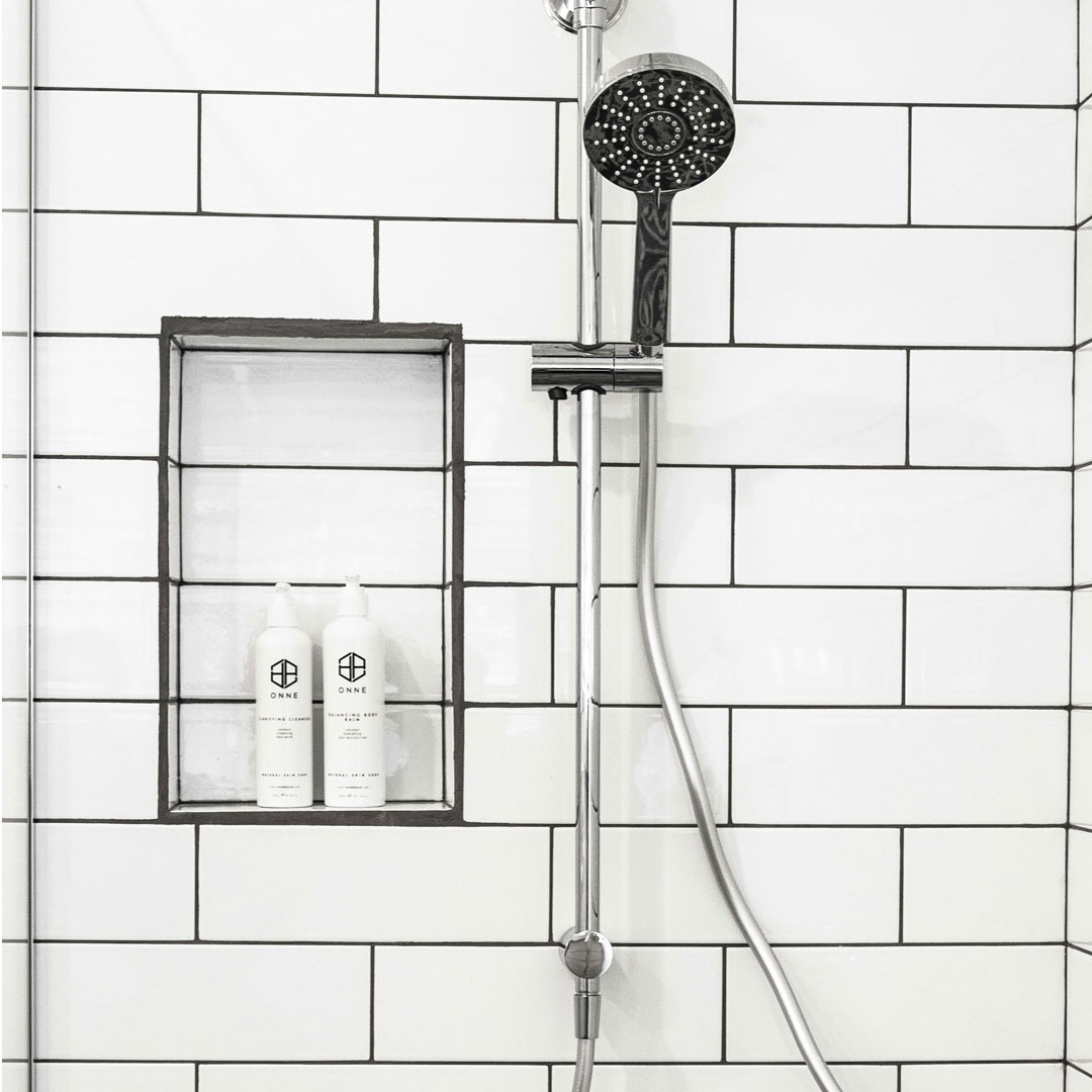 white-shower-unsplash-square Kitchen sink with white countertops, black faucet and wooden cutting board.